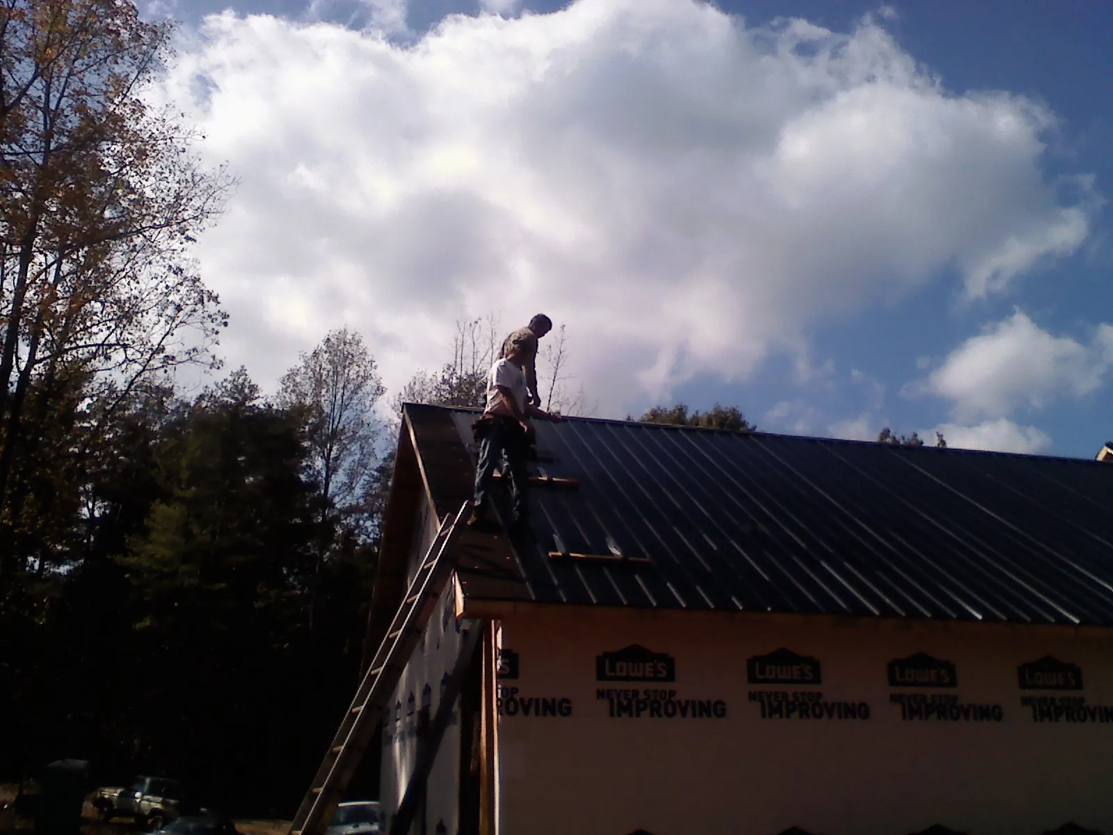 Roofer fastening dark metal panels high against a cloudy sky, from a Roof Inspection job in Mount Sterling